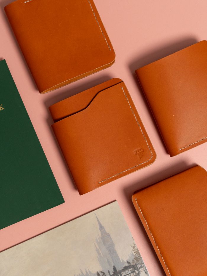 Overhead view of orange leather wallets paired with books on a pink backdrop.